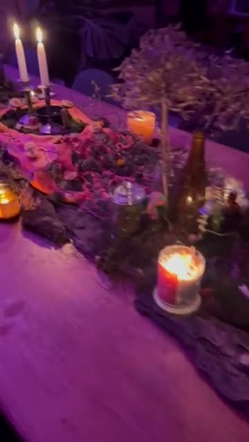 Candlelit tablescape of moss, bark, dried flowers and candles under purple light