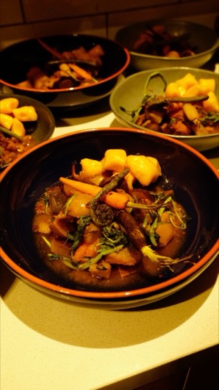Bowls of flash boil up: a dark broth with baby carrots, fern fronds, greens and golden dumplings